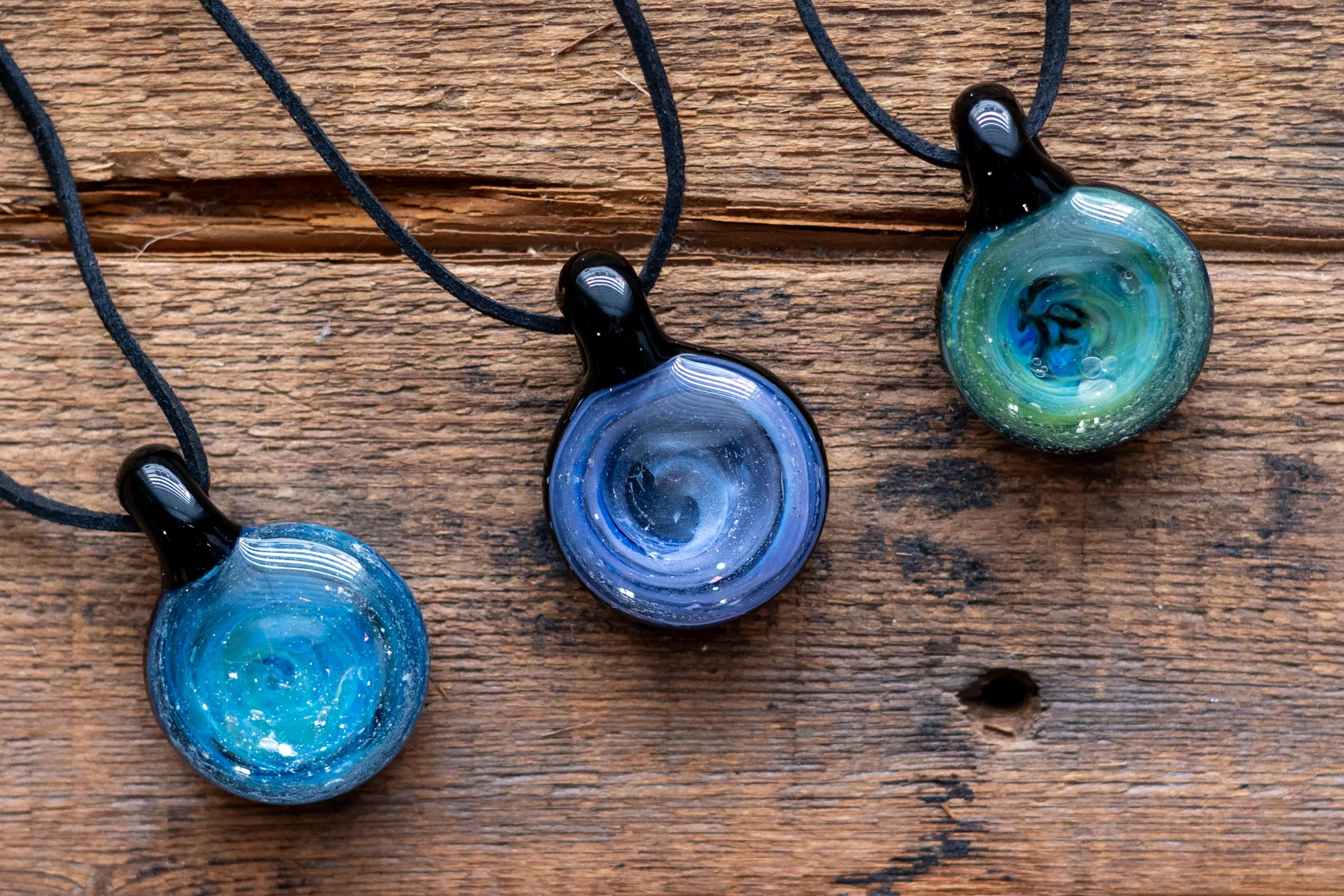 three blue and green glass pendants hanging from black cord